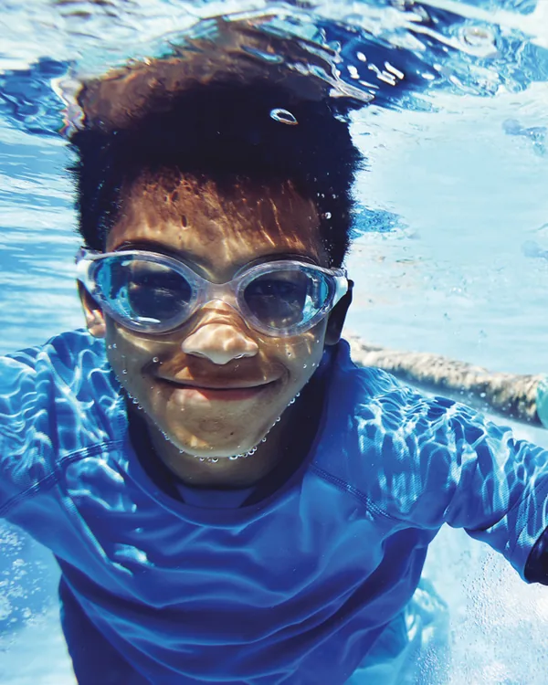 A boy in goggles smiling under water in a swimming pool