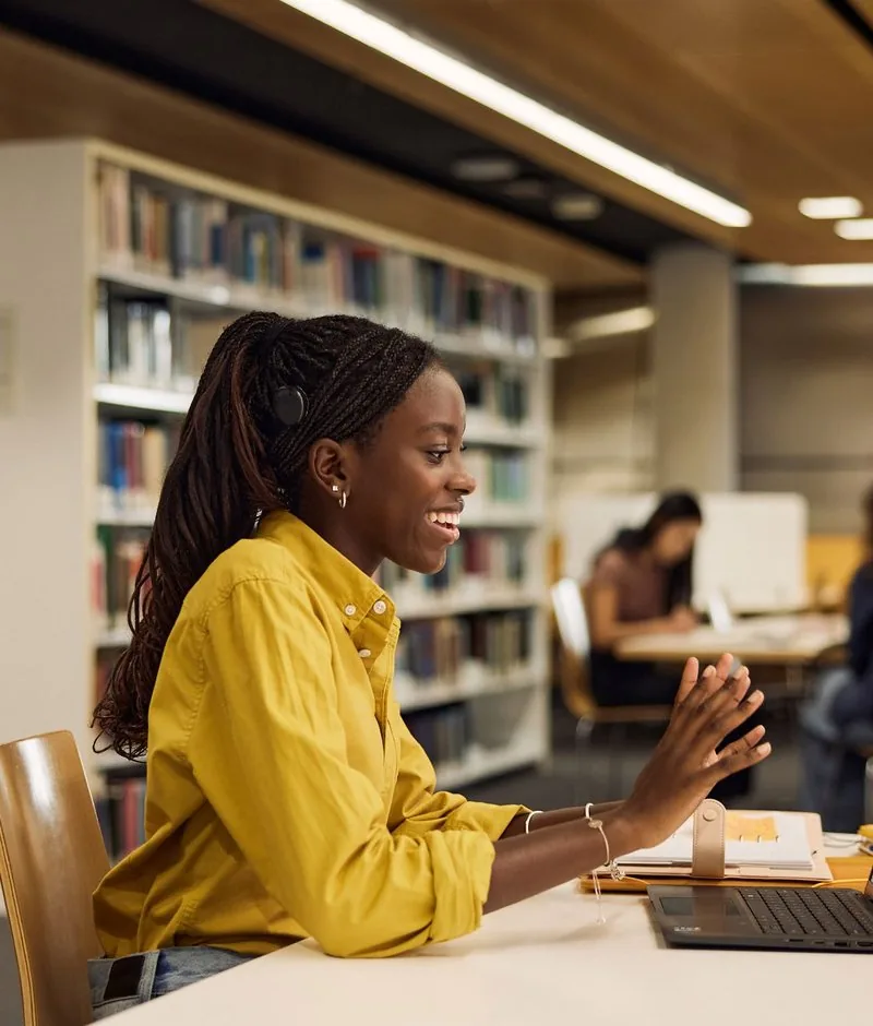 A smiling woman wearing a Cochlear sound processor, talking at a desk in a library