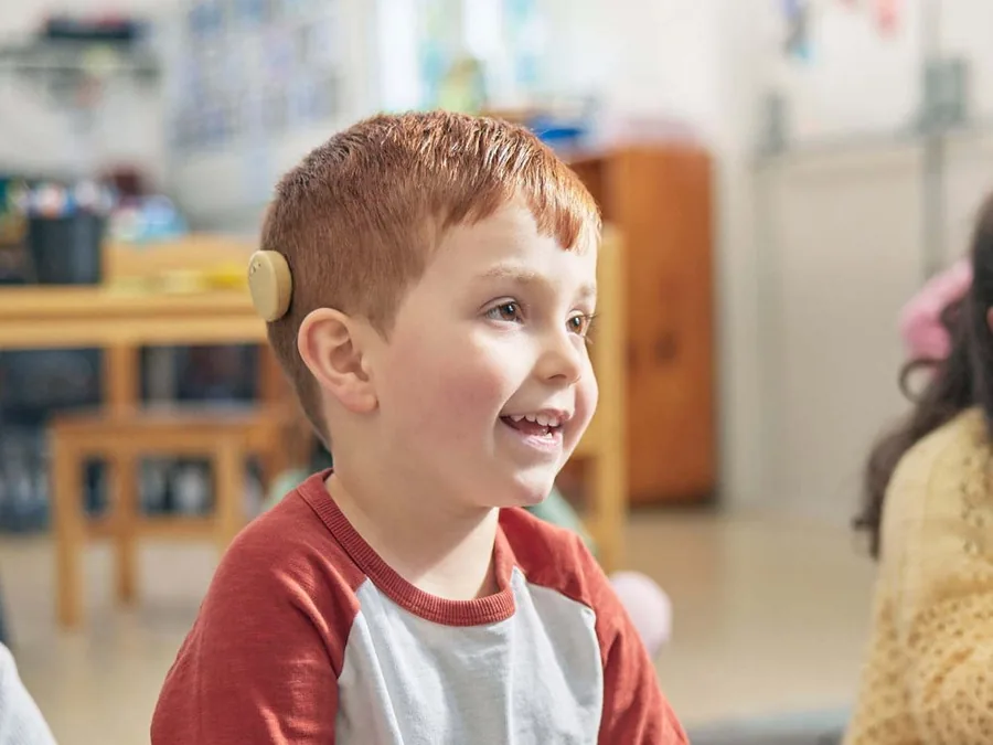 A young boy in a classroom wearing a Cochlear off-the-ear sound processor