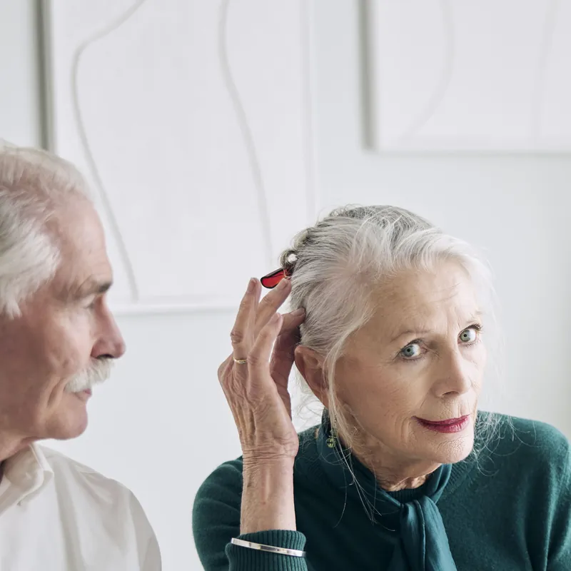 An older woman touching her ear while talking with her husband