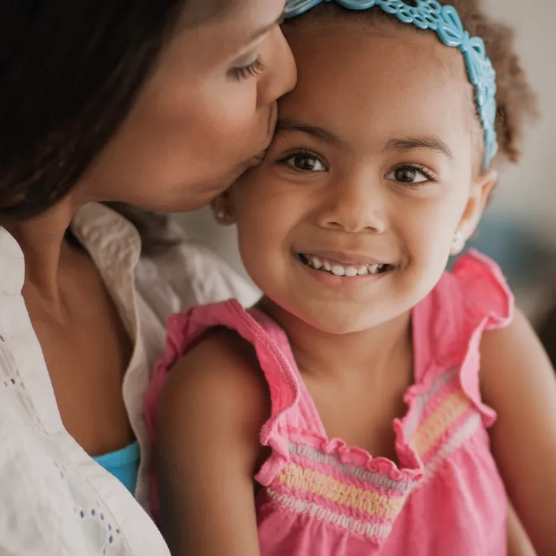 A mother kissing her smiling young daughter on the cheek